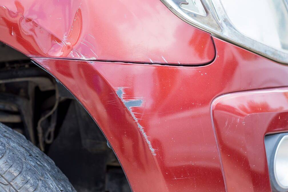 red car with dents and scrapes in need of collision repair